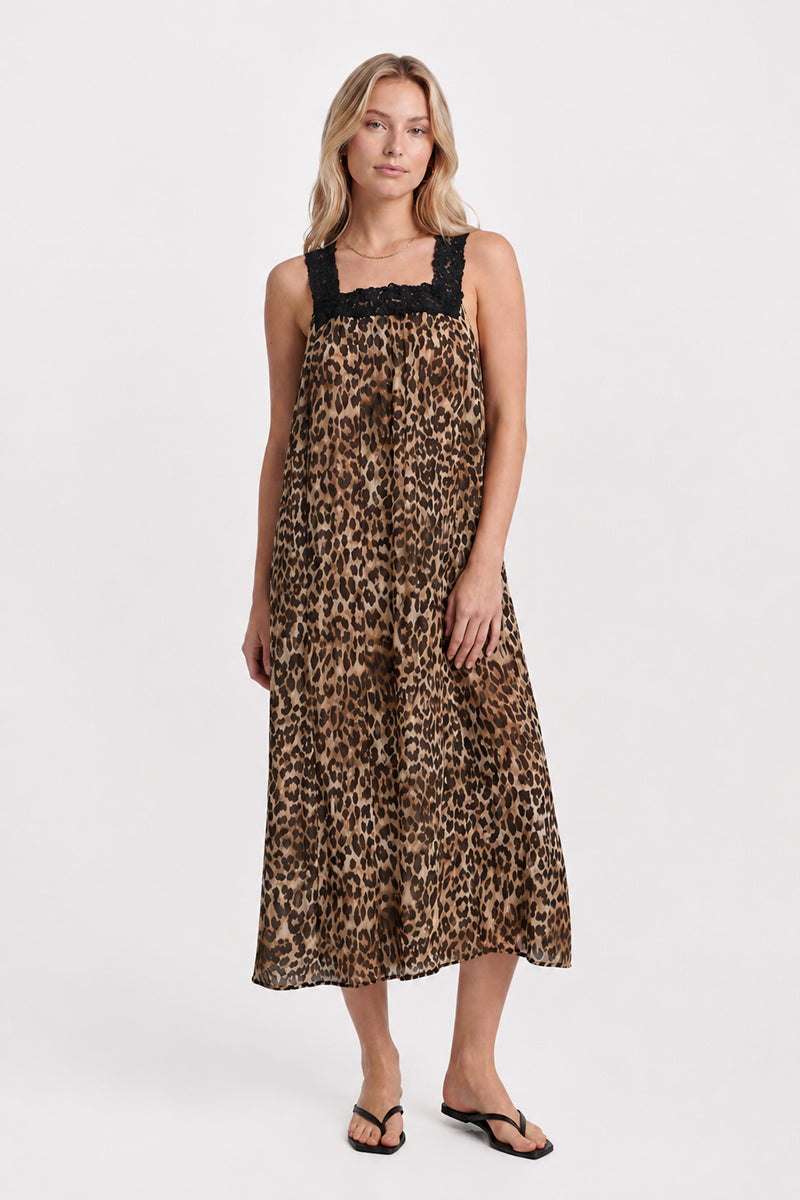 Eine Frau steht in einem ärmellosen Maxikleid mit Leopardenmuster von „Princess Goes Hollywood“, das mit zarten schwarzen Spitzen-Trägern versehen ist. Sie hat langes blondes Haar, einen ausdruckslosen Gesichtsausdruck und trägt schwarze Flip-Flops. Der Hintergrund ist schlicht weiß.
