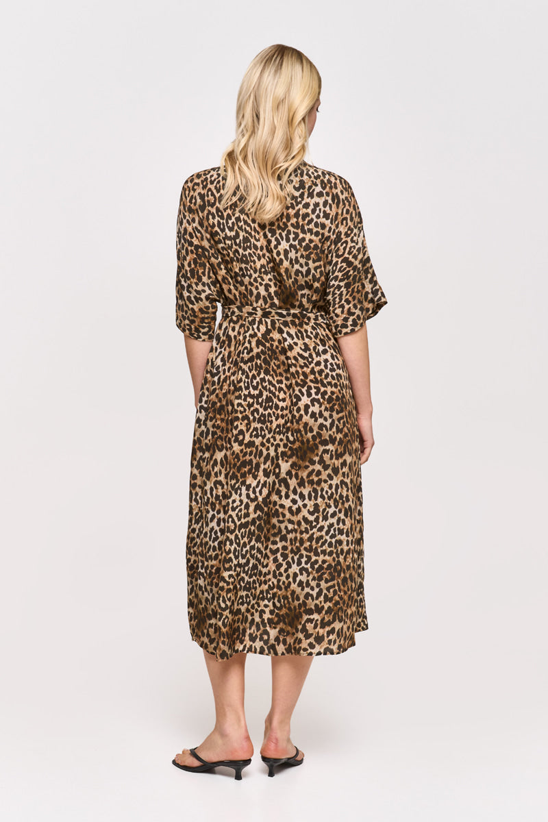 Eine Frau mit langen blonden Haaren trägt ein Princess Goes Hollywood Leoprint Hemdblusenkleid mit Taillengürtel, kurzen Ärmeln und einem schicken braun-schwarzen Leopardenmuster auf weißem Grund, gepaart mit schwarzen, offenen, niedrighackigen Sandalen.