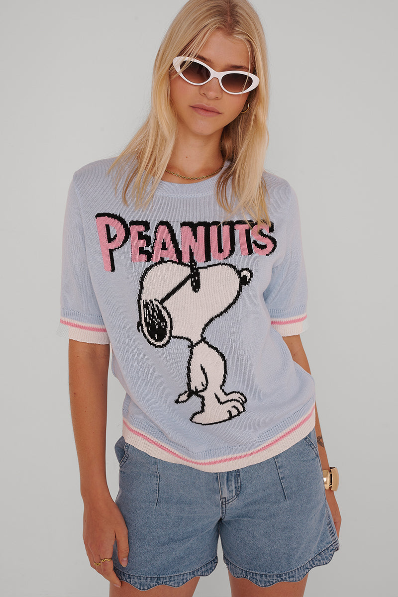 Eine Frau mit glattem blondem Haar trägt eine weiße Sonnenbrille mit Katzenaugen, ein hellblaues Snoopy "PEANUTS"-Strickoberteil und Jeansshorts mit elastischem Bund von Princess Goes Hollywood. Sie steht vor einem schlichten hellgrauen Hintergrund und blickt zur Seite.