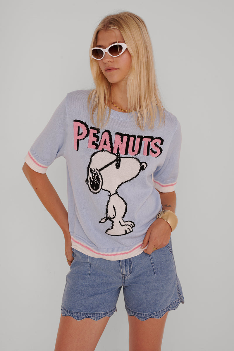 Eine Person mit langen blonden Haaren trägt eine weiße Cat-Eye-Sonnenbrille, Denim-Shorts und einen Princess Goes Hollywood Peanuts Pullover aus Baumwollmix mit Snoopy-Motiv. Sie posiert vor einem hellgrauen Hintergrund, eine Hand in der Tasche, die andere an der Hüfte.