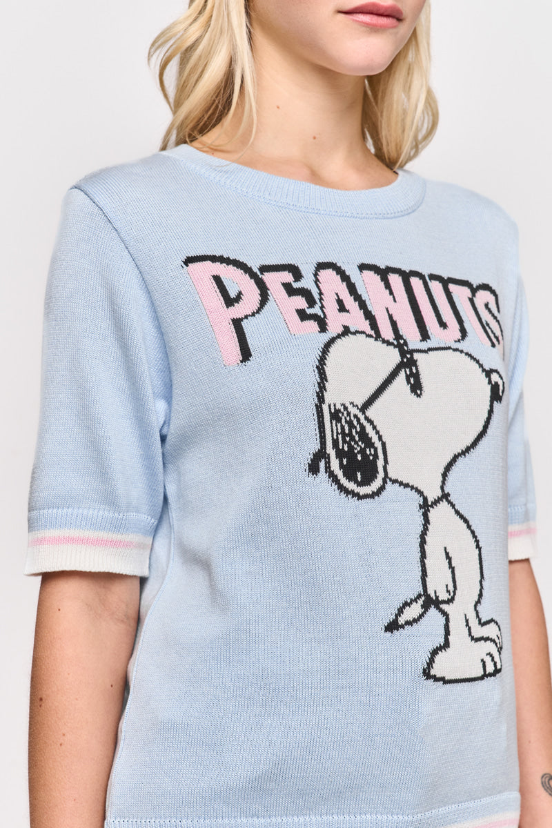 Eine Frau mit gewellten blonden Haaren trägt einen hellblauen Princess Goes Hollywood Peanuts-Pullover von Baumwollmix mit einem großen Snoopy-Motiv, einem auffälligen rosa-schwarzen PEANUTS-Schriftzug und einer weiß-rosa Borte an den Ärmeln. Nur die untere Hälfte des Gesichts ist sichtbar.