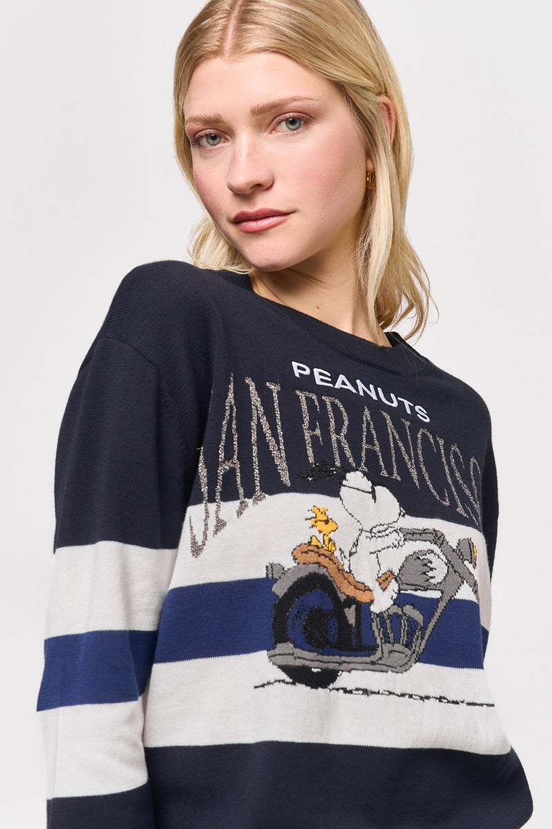 Eine junge Frau mit heller Haut und blondem Haar trägt einen marineblauen Princess Goes Hollywood Baumwolle-Kaschmir-Pullover mit einem Peanuts-Snoopy-Motiv, das weiß und blau gestreift ist. Sie blickt nach vorne und schaut leicht zur Seite.