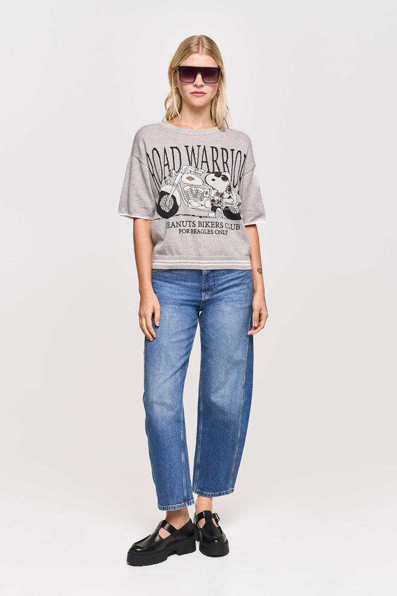 Eine Frau mit glattem blondem Haar und einer entspannten, selbstbewussten Haltung steht vor einem weißen Hintergrund und trägt eine rosa Sonnenbrille, ein lockeres graues Princess Goes Hollywood ROAD WARRIOR Snoopy Grafik-T-Shirt, blaue Jeans mit geradem Bein und schwarze Plateausandalen.