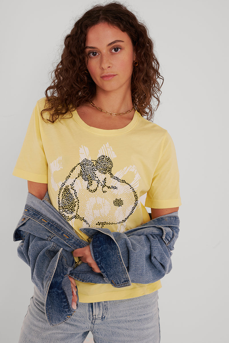 Eine Person mit langen lockigen Haaren trägt ein gelbes Princess Goes Hollywood Baumwolle-T-Shirt mit Paillettenmotiv und eine hellblaue Jeansjacke, die sie über die Arme gelegt hat, und blickt nach vorne auf einen schlichten weißen Hintergrund.