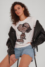 Eine Person mit lockigem braunem Haar trägt ein Princess Goes Hollywood T-Shirt mit Leoprint und Snoopy, hellblaue Jeansshorts und eine schwarze Lederjacke. Sie sitzt auf einem Hocker vor einem schlichten Hintergrund und blickt selbstbewusst in die Kamera.