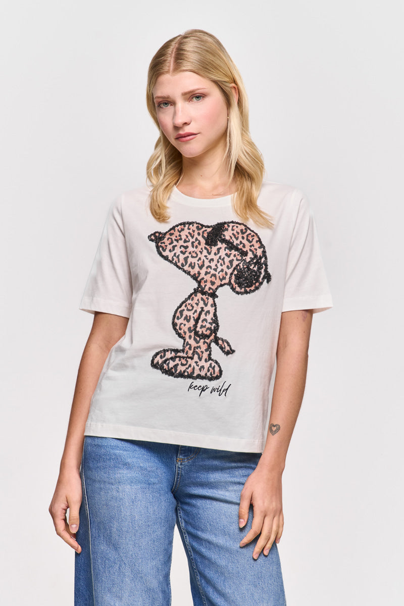 Eine junge blonde Frau trägt ein Princess Goes Hollywood Snoopy T-Shirt mit einem fetten Leoprint Snoopy und dem Slogan "keep wild", gepaart mit blauen Jeans, während sie vor einem schlichten Hintergrund steht.
