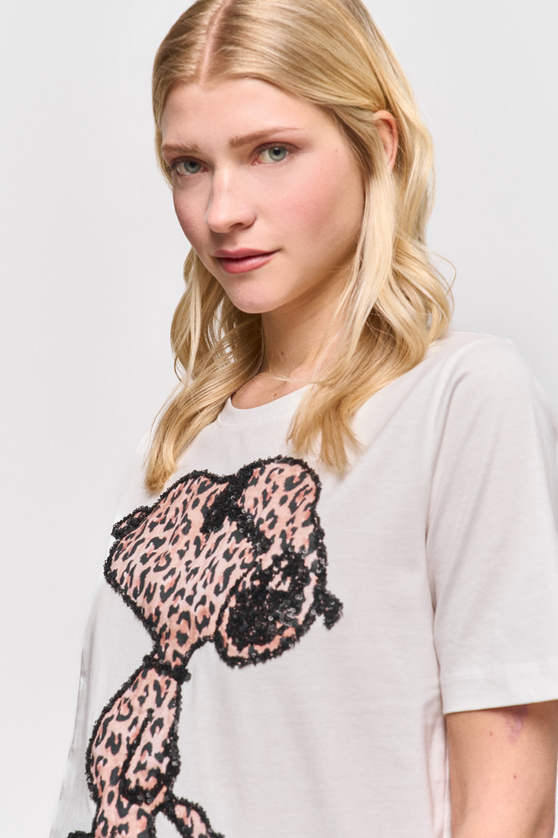 Eine Frau mit heller Haut und langen blonden Haaren steht vor einem weißen Hintergrund, trägt ein Princess Goes Hollywood Snoopy T-Shirt aus Baumwolle mit einer großen rosa Leoprint-Grafik und blickt mit sanftem Ausdruck leicht zur Seite.