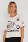 Eine junge Frau mit glattem blondem Haar trägt ein übergroßes Princess Goes Hollywood Snoopy T-Shirt aus Baumwolle, auf dem Snoopy auf einem Motorrad, der Schriftzug ROAD WARRIOR, ein Route 66-Schild und schwarze Jeans vor einem schlichten hellen Hintergrund zu sehen sind.