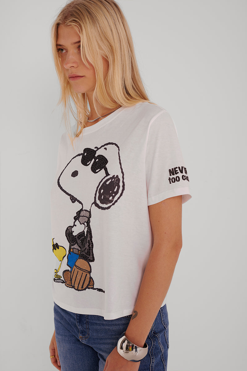 Eine junge Frau mit langen blonden Haaren trägt ein Princess Goes Hollywood Snoopy-T-Shirt, auf dem Snoopy mit Sonnenbrille abgebildet ist, der sich mit Woodstock auf einen Basketball stützt. Auf dem Ärmel ist "NEVER TOO COOL" aufgedruckt. Dazu trägt sie eine blaue Jeans und eine weiße Uhr.