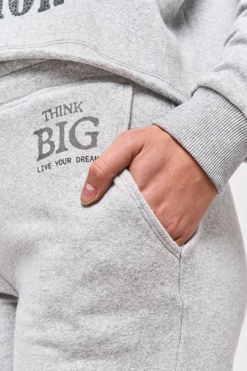 Nahaufnahme einer Person in hellgrauen Sweat-Bermudashorts und passendem Sweatshirt von Princess Goes Hollywood. Ihre rechte Hand steckt in der Tasche, neben der Tasche ist in Grau "THINK BIG LIVE YOUR DREAM" aufgedruckt.