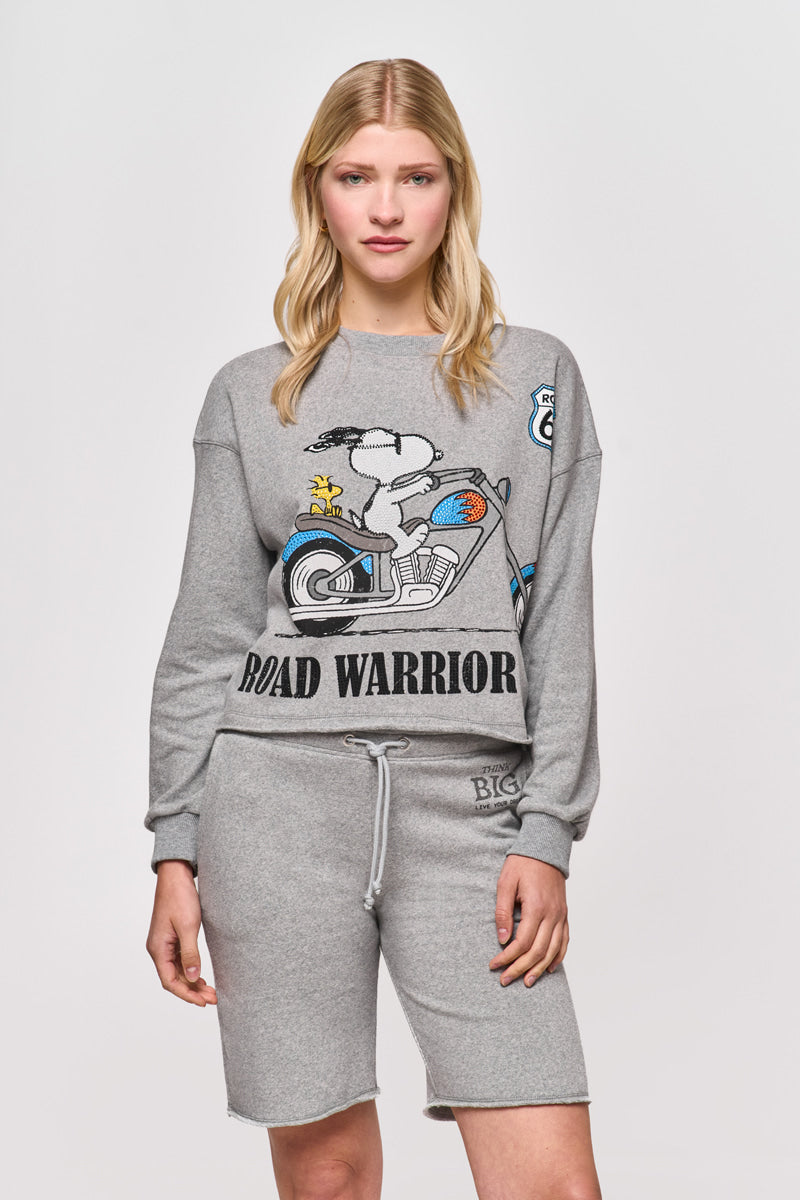 Eine Frau mit langen blonden Haaren trägt eine graue Princess Goes Hollywood Sweat-Bermudashorts mit elastischem Bund und ein passendes Sweatshirt mit Snoopy, Woodstock auf einem Motorrad und dem Schriftzug "ROAD WARRIOR" vor einem schlichten hellen Hintergrund.