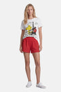 Eine Frau mit langen blonden Haaren trägt ein weißes T-Shirt mit Woodstock-Aufdruck in limitierter Auflage von Princess Goes Hollywood, dazu weite rote Shorts und weiße Low-Top-Sneaker; sie steht vor einem schlichten weißen Hintergrund.