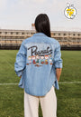 A person stands on grass with their back to the camera, wearing a Princess Goes Hollywood light blue denim jacket featuring Peanuts in large script and cartoon characters below. A Peanuts 75th Anniversary logo appears in the top right corner.