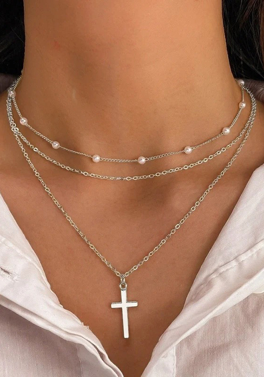 Close-up of a neck wearing layered Princess Goes Hollywood Halskette in Silberoptik: a short chain with small pearls and a longer chain with silver Kreuzanhänger. A white collared shirt is partially visible at the bottom.