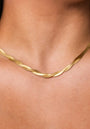 A close-up of a neck wearing Princess Goes Hollywood’s flat, twisted Gliederkette in 18K gold plating. The necklace sits smoothly on the skin, with a subtle wave pattern, keeping all attention on this elegant piece against a neutral background.