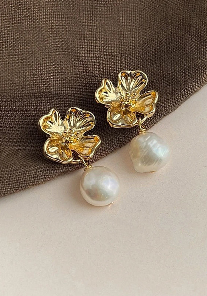 A pair of gold flower-shaped Ohrstecker by Princess Goes Hollywood, with intricate petals and sparkling centers, each featuring a dangling runde Süsswasserperle, displayed on brown textured fabric.