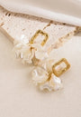 A pair of Princess Goes Hollywood gold Ohrstecker with textured rectangular Edelstahl studs and dangling wavy, iridescent white Kunstperlen, resembling flower petals, displayed on light beige stone with soft white fabric above.
