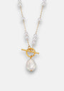 A Princess Goes Hollywood necklace with an 18K gold-plated chain, small white freshwater pearls, a gold toggle clasp, and a large irregular white pearl pendant, displayed on a light gray background.