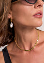 A woman with short brown hair, natural makeup, and a black top wears black sunglasses, a gold twisted necklace, and Princess Goes Hollywood Creolen Edelstahl with dangling Süsswasserperle. The photo highlights her neck and accessories.