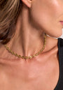 A close-up of a woman’s neck and jawline, wearing the Princess Goes Hollywood Statement-Halskette aus Muschelgliedern mit 18K Goldbeschichtung. The elegant necklace rests on her collarbone, paired with a black top and brown hair.