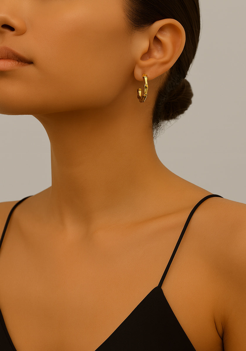 A woman with smooth, medium skin and dark hair in a low bun wears a black spaghetti strap top by Princess Goes Hollywood and chunky vergoldete Creolen. Only her lower face, neck, and part of her shoulder appear against a neutral background.