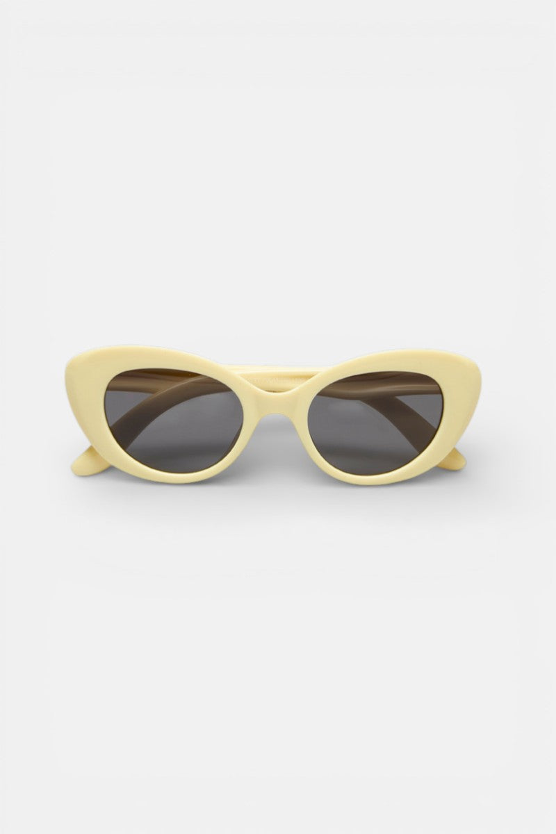 Die Cat-Eye-Sonnenbrille Okkia mit ihrem dicken, hellgelben Rahmen und den dunkel getönten Gläsern steht auf einem einfarbig weißen Hintergrund und ist dem Betrachter zugewandt.