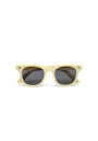 Front view of an Okkia Kinder-Sonnenbrille with thick pale yellow frames, dark oval lenses, and small black cross-shaped details. Made from flexible TPEE material for reliable protection. Shown on a plain white background.