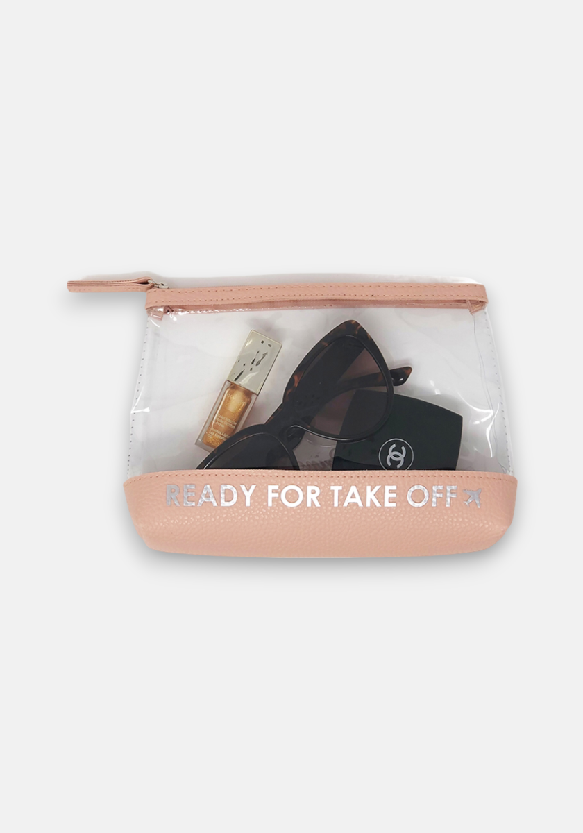 The Princess Goes Hollywood Travel Kit by Princess Goes Hollywood is a clear zipper pouch with pink trim and READY FOR TAKE OFF in white. It holds black sunglasses, a Chanel compact, and a small gold perfume bottle, set against a plain light gray background.