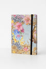 A decorative Princess Goes Hollywood Jahresplaner 2026 stands upright against a white background, featuring colorful flowers, gold baroque patterns, a subtle leopard print, and a black elastic band closure along the right edge.