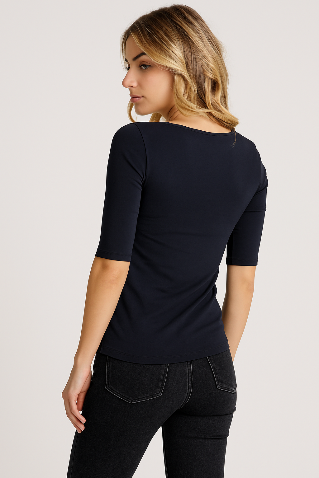 Eine Frau mit gewelltem blondem Haar blickt über ihre Schulter. Sie trägt ein tailliertes 3/4-Arm-Baumwollhemd von Princess Goes Hollywood in Marineblau und schwarze Jeans. Sie steht vor einem hellen Hintergrund, der die Rückseite und die Seite ihres Outfits zeigt.