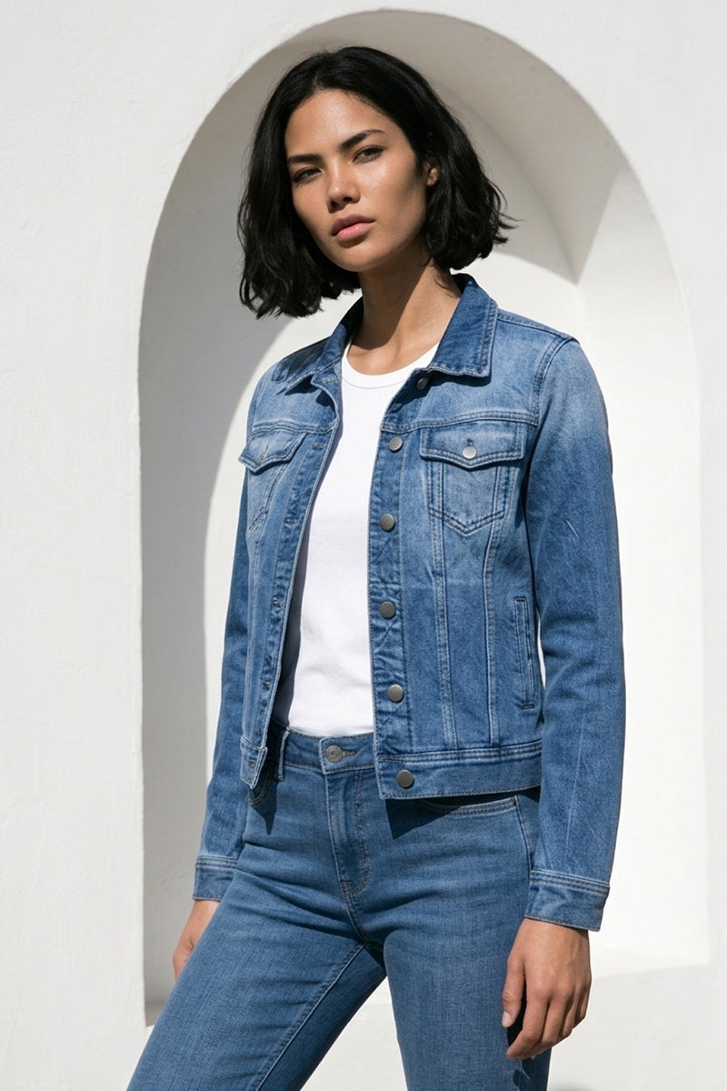 Eine Frau mit kurzen dunklen Haaren steht vor einer weißen, gewölbten Wand. Sie trägt ein blaues Princess Goes Hollywood Damen Hemd aus Baumwolle über einem weißen T-Shirt und einer passenden Jeans und blickt selbstbewusst und mit neutralem Blick in die Kamera.