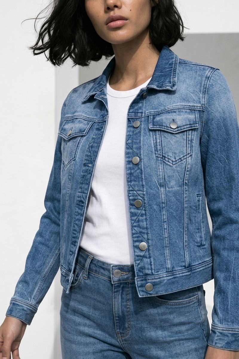 Eine Person mit kurzen, gewellten dunklen Haaren trägt ein hellblaues Princess Goes Hollywood Damen Hemd aus Baumwolle über einem weißen T-Shirt und einer dazu passenden Denim-Jeans. Die Jacke hat Metallknöpfe, zwei Brusttaschen, und nur das untere Gesicht und der Oberkörper sind sichtbar.