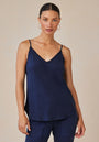 A woman with slicked-back dark hair wears a Bella Dahl navy Lyocell V-neck camisole featuring thin straps and frayed edges, paired with matching pants. She stands facing the camera with a neutral expression against a plain beige background.