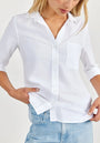 A woman in a crisp white Bella Dahl Hemdbluse with chest pocket and rolled-up sleeves, styled oversized, pairs it with light blue jeans. Her blonde hair falls loosely as she slips a hand into her pocket. The shirt is made from 100% Lyocell.