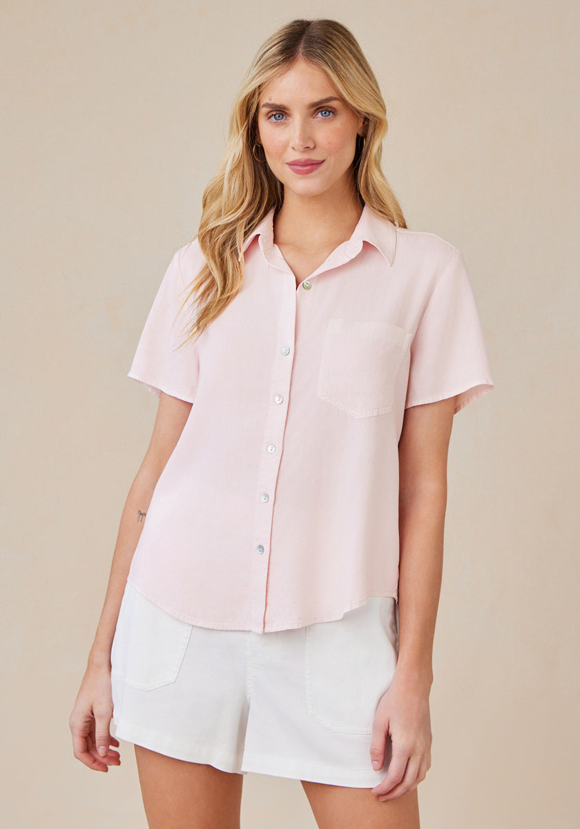 A woman with long blonde hair models a light pink Bella Dahl Lyocell blouse with a Hemdkragen and chest pocket, paired with white shorts. She stands facing forward, lightly smiling against a beige background.