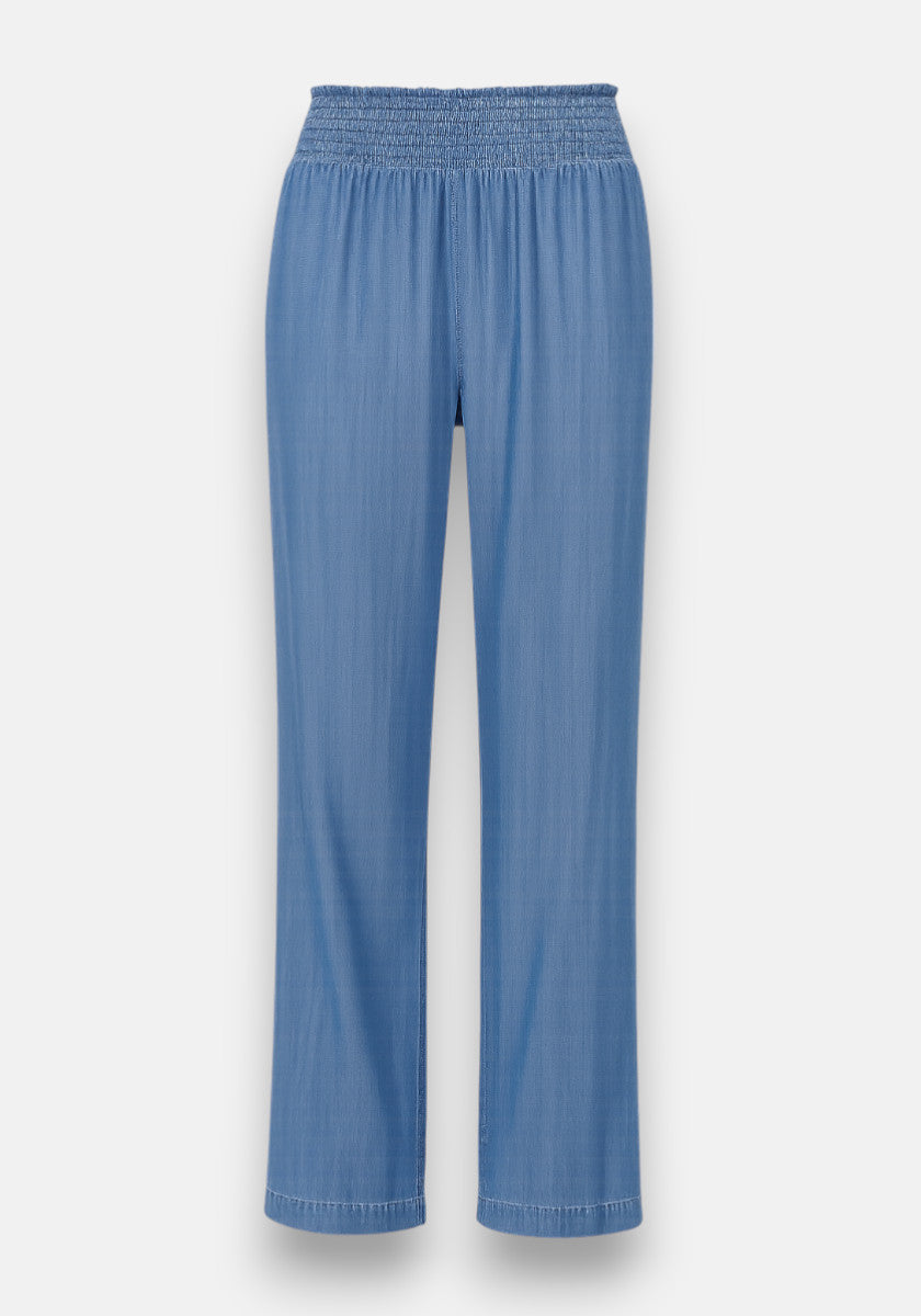 Bella Dahl’s light blue Lyocel wide-leg pants feature a denim-look, soft lightweight fabric, high smocked elastic waistband, relaxed fit, and straight hems. The subtly textured material stands out against a plain white background.