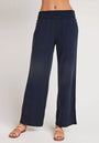 A person wears loose-fitting, navy blue wide-leg Bella Dahl Hose in Denimoptik with a smocked elastic waistband and flat beige sandals with thin straps. The upper body is not visible against a plain, light-colored background.
