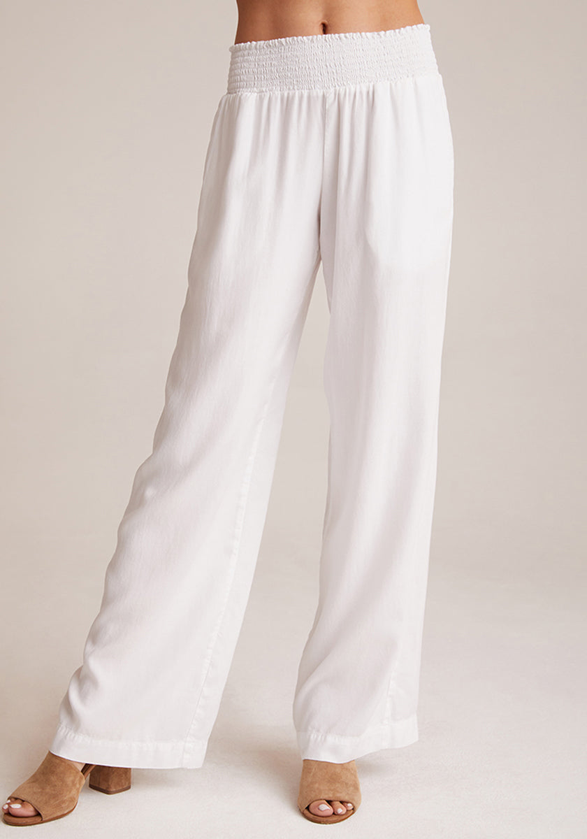 A person wears Bella Dahl’s loose, white wide-leg pants in Denimoptik with a smocked elastic waistband, paired with tan open-toe heeled sandals. The image is cropped from the waist down against a plain light background.