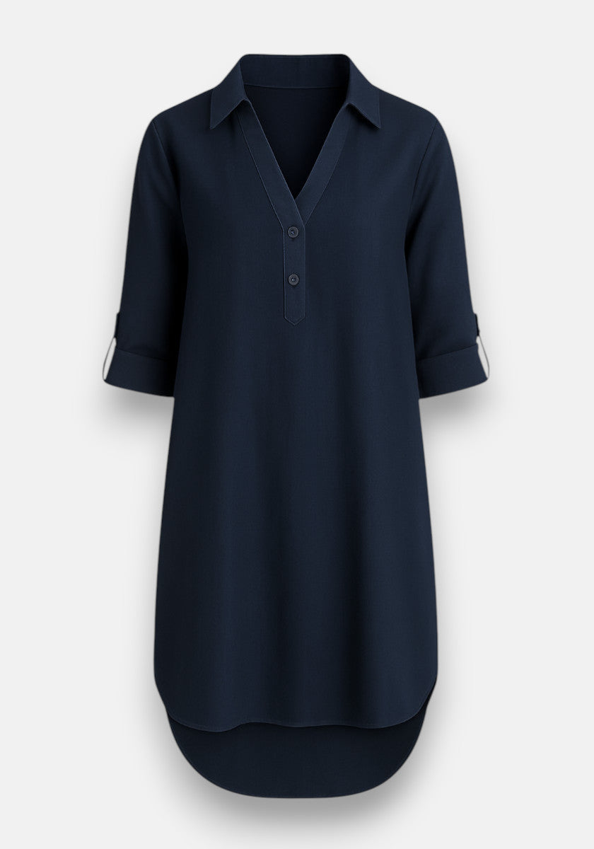 A navy blue Lyocell dress by Bella Dahl with a collared V-neck, partial button placket, and three-quarter sleeves rolled with buttoned tabs. The knee-length hem is slightly rounded and longer at the back. Light gray background.