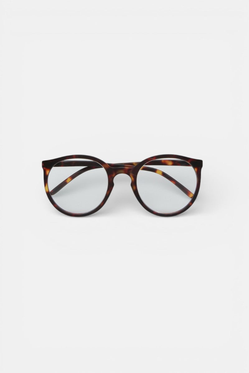 Eine Okkia Lesebrille mit rundem Design und dünnem schildpattgemusterten Rahmen ist auf einem schlichten weißen Hintergrund zentriert. Die Brille bietet ein komfortables Tragegefühl, mit dezenten Braun-Amber-Tönen und leicht nach außen gewinkelten Bügeln.