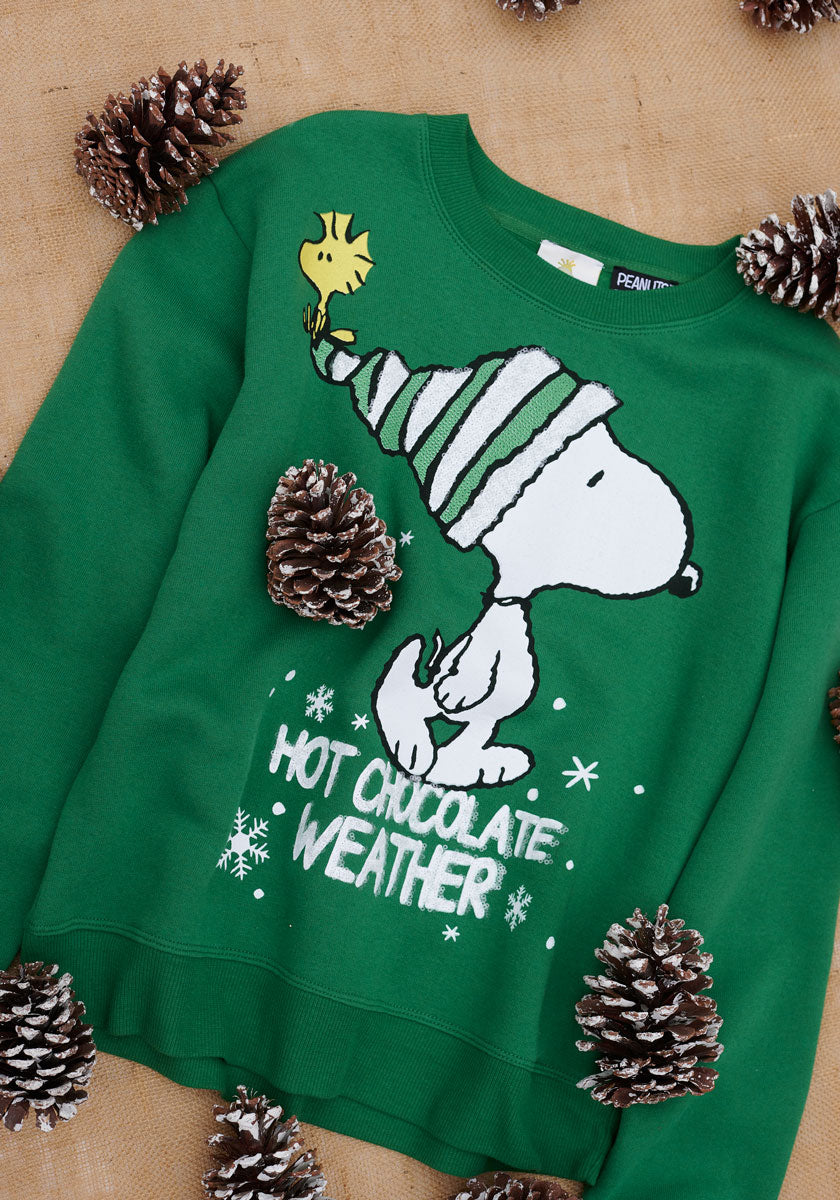Der festliche grüne Snoopy-Pullover von Princess Goes Hollywood zeigt Snoopy in einer gestreiften Mütze mit Woodstock- und "Hot Chocolate Weather"-Schriftzug sowie Schneeflocken für gemütliche Weihnachtsstimmung - perfekt für die Weihnachtszeit.