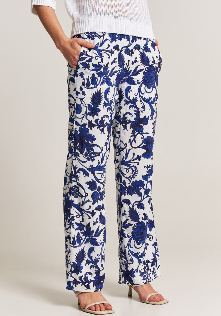 A person wears Princess Goes Hollywood white floral-print, wide-leg pants with elastic waistband and pockets, paired with a white knit sweater and open-toe heeled sandals. The plain background keeps the focus on the outfit; face not shown.