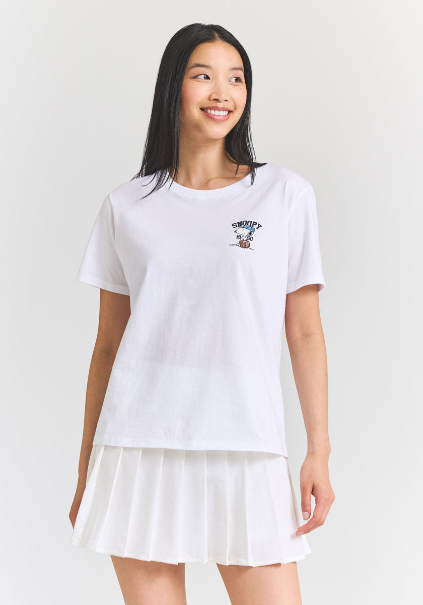 A young woman with straight, long black hair smiles in a Princess Goes Hollywood white Snoopy T-shirt with subtle Strassverzierung on the left chest, paired with a white pleated skirt against a plain, well-lit background.