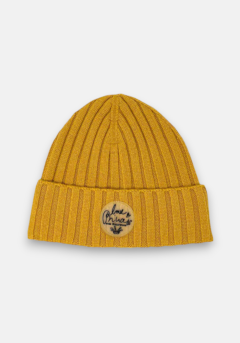 A mustard yellow beanie by Princess Goes Hollywood with colorful knit details and a ribbed design. The folded brim has a round beige love Brinca patch with a black heart and leaf. Shown on a white background.