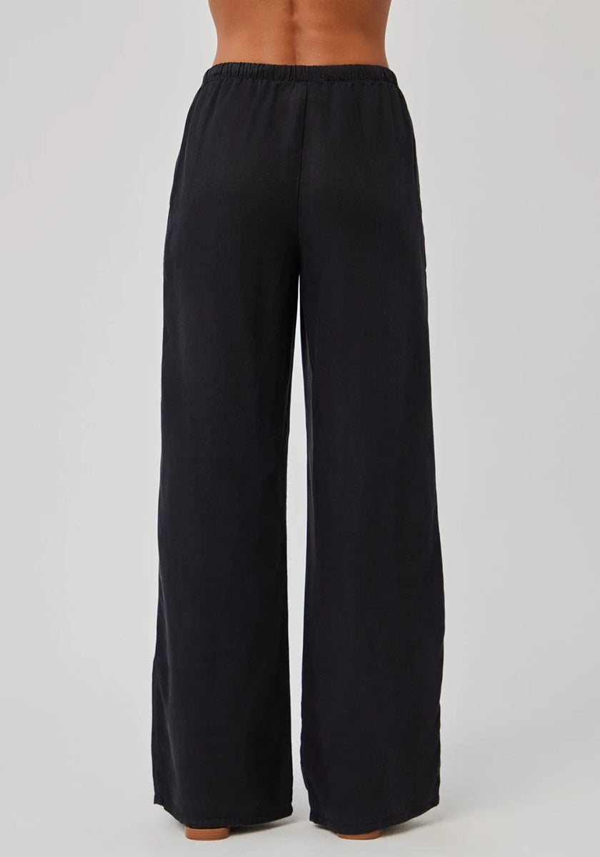 A person is shown from the waist down, wearing black high-waisted, wide-leg Lyocell pants with an elastic waistband from Bella Dahl. The soft, flowing fabric stands out against a plain, light-colored background.
