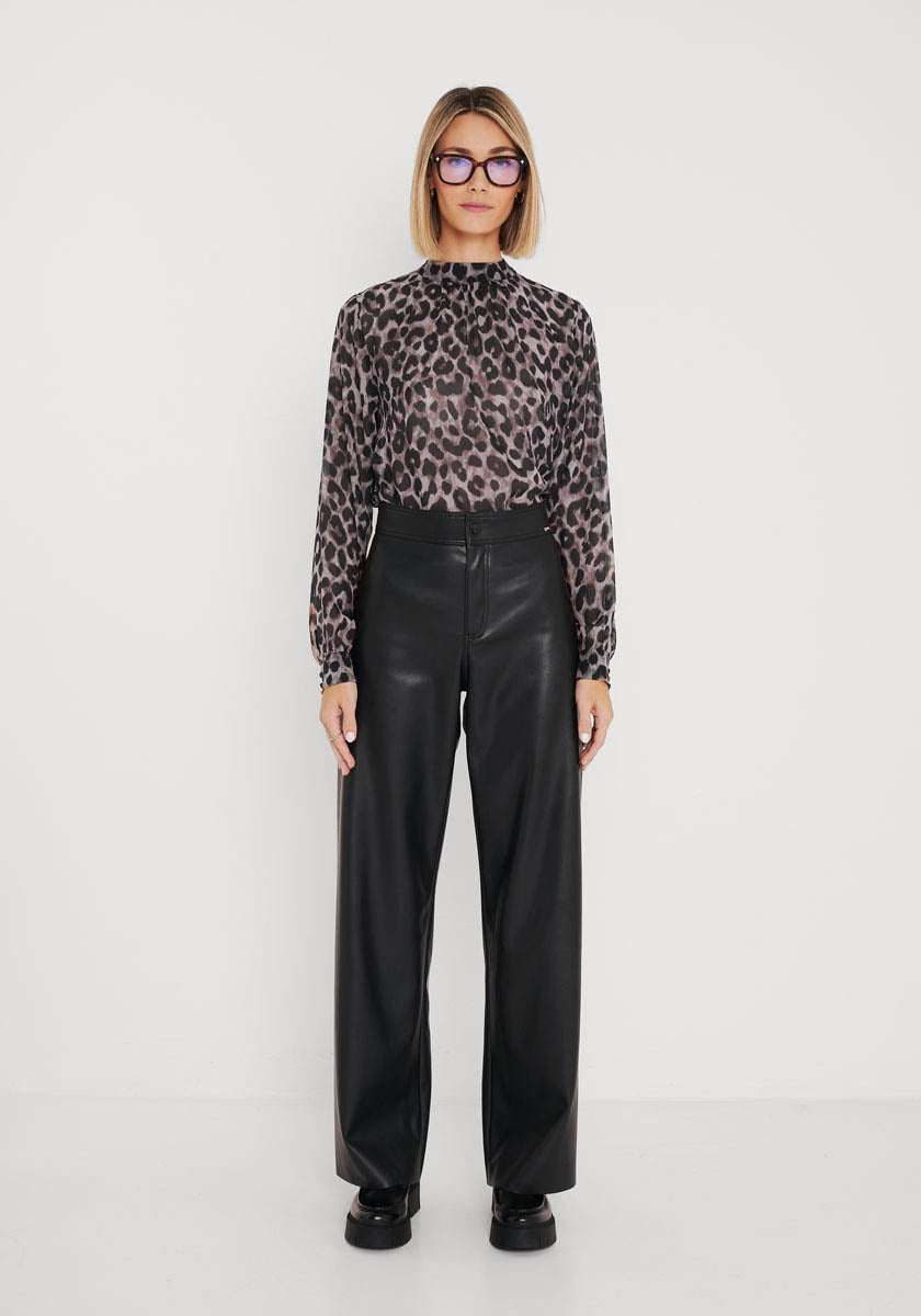 Eine Frau mit glattem blondem Haar und Brille trägt eine langärmelige, transparente Bluse mit Wild-Leo-Print und eine hochtaillierte, schwarze Lederhose mit weitem Bein von Princess Goes Hollywood und steht vor einem einfarbig weißen Hintergrund.