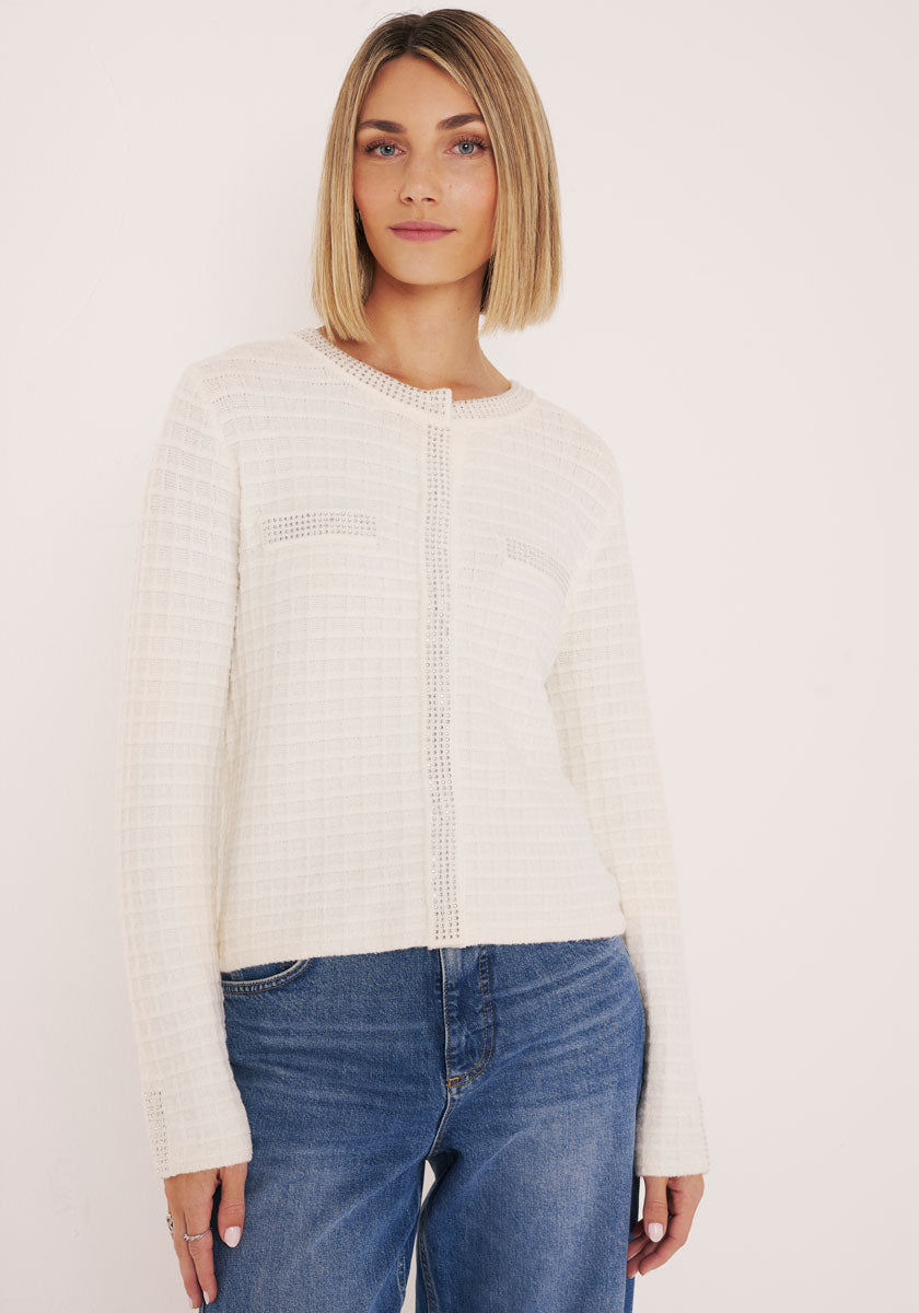 Eine Frau mit blondem Bob trägt ein strukturiertes, cremefarbenes, langärmeliges Oberteil aus weichem Baumwolle-Kaschmir-Mix von Princess Goes Hollywood mit dezenten vertikalen Details, kombiniert mit einer mittelhohen blauen Jeans vor einem schlichten, hellen Hintergrund.