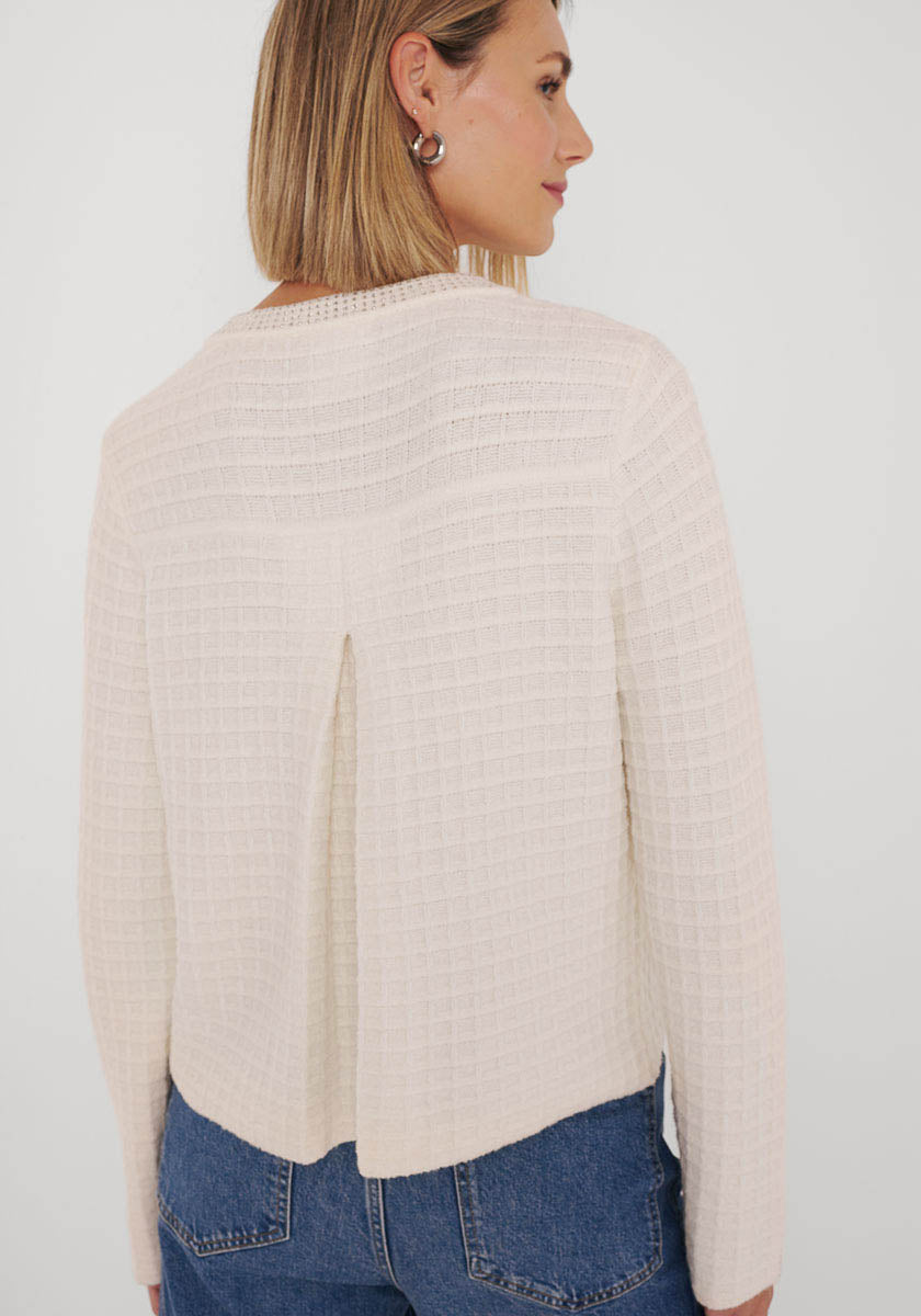 Eine Frau mit glattem blondem Haar modelliert die Rückseite einer strukturierten, cremefarbenen Princess Goes Hollywood-Strickjacke aus Baumwolle und Kaschmir, die eine Mittelfalte aufweist. Sie trägt silberne Reifchen und blaue Jeans vor einem schlichten weißen Hintergrund.