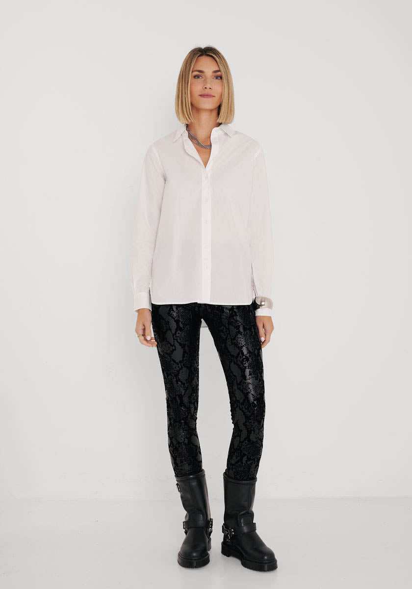 Eine Frau mit glattem, schulterlangem blondem Haar steht vor einem weißen Hintergrund. Sie trägt ein weißes Button-up-Hemd, eine Kunstleder-Leggings mit elastischer Taille im Schlangenmuster von Princess Goes Hollywood und schwarze Stiefel. Sie blickt direkt in die Kamera.