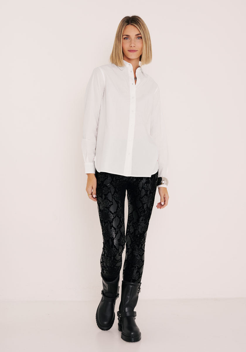 Eine Frau mit blondem Bob modelliert das weiße Button-up-Shirt von Princess Goes Hollywood und die schwarze Kunstleder-Leggings mit Schlangendruck und elastischer Taille, kombiniert mit schwarzen Ankle Boots. Sie steht entspannt mit dem Blick nach vorne vor einem schlichten, hellen Hintergrund.